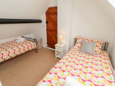 A bedroom with two single beds a nightstand with a lamp and a wooden door at Old Stable Cottage in Alnmouth