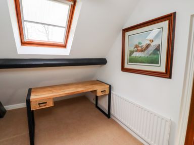 A small room with a wooden desk under a skylight and a framed picture of horse racing on the wall at Old Stable Cottage in Alnmouth