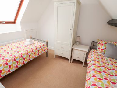 A bedroom with two single beds a white wardrobe and a bedside table at Old Stable Cottage in Alnmouth