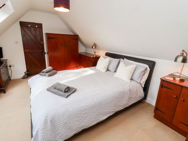 A bedroom with a bed and folded towels on it wooden cabinets a wooden door and bedside lamps at Old Stable Cottage in Alnmouth