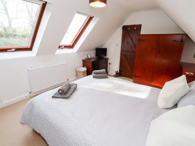 A bedroom with a bed, towels, a wooden wardrobe, a small dresser with a TV, and two skylight windows at Old Stable Cottage in Alnmouth