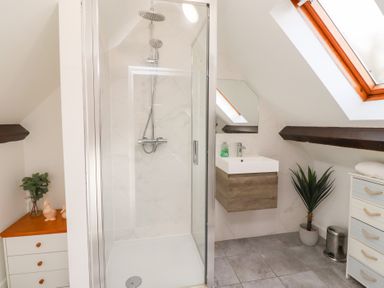 A bathroom with a glass shower enclosure, wall-mounted sink, skylight window, and cabinets at Old Stable Cottage in Alnmouth
