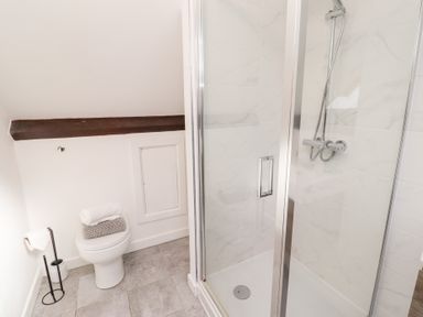 A bathroom with a toilet and a glass shower enclosure at Old Stable Cottage in Alnmouth