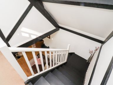 A staircase with black steps and white railing leading to a living area with a sofa and wooden floor at Old Stable Cottage in Alnmouth