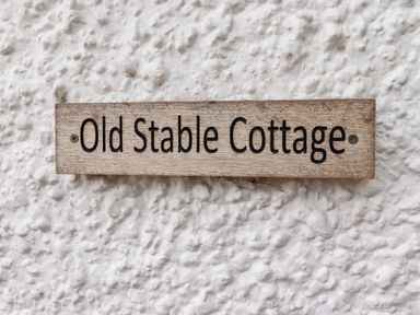 A wooden sign with Old Stable Cottage text on a textured white wall at Old Stable Cottage in Alnmouth