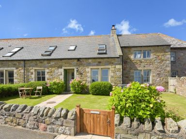 A stone cottage with skylights and a small garden with a wooden gate and outdoor table at Ottoline Cottage in Embleton