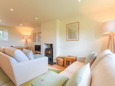 A living room with two sofas a wood-burning stove a basket with firewood lamps and a dining table at Ottoline Cottage in Embleton