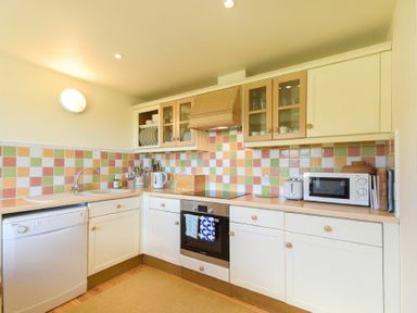 A kitchen with colorful tiled backsplash white cabinets a dishwasher oven microwave and kettle at Ottoline Cottage in Embleton