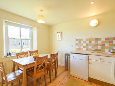 A kitchen with wooden dining table and chairs and a dishwasher under a counter at Ottoline Cottage in Embleton