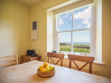 A dining area with wooden chairs and a table with a bowl of fruit near a window showing a countryside view at Ottoline Cottage in Embleton