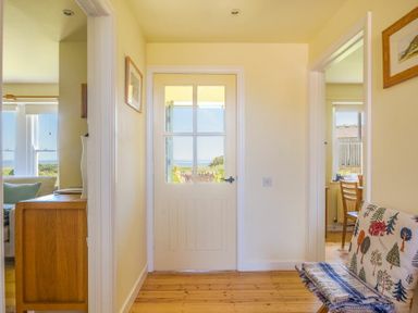 A hallway with wooden floor a door with glass panels and rooms on each side at Ottoline Cottage in Embleton