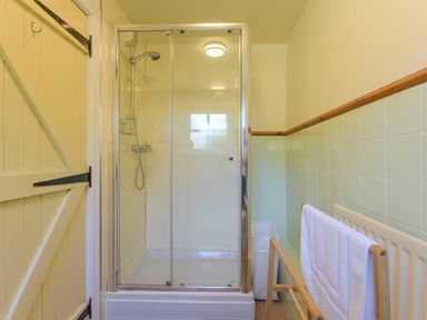 A bathroom with a shower enclosure a wooden towel rack with a white towel and a wooden door at Ottoline Cottage in Embleton