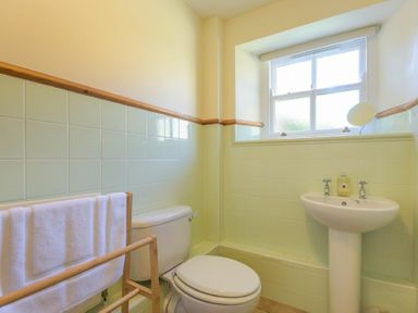 A bathroom with a toilet a pedestal sink a window and a wooden towel rack with towels at Ottoline Cottage in Embleton