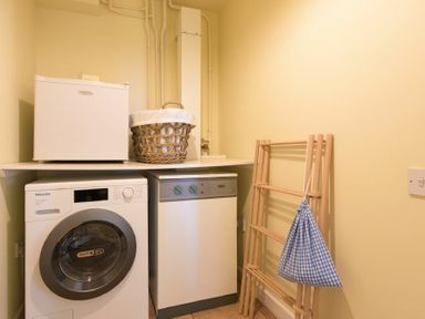 A laundry room with a washing machine dryer dishwasher and drying rack at Ottoline Cottage in Embleton