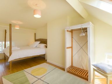 A bedroom with a four-poster bed a fabric wardrobe a chair with a cushion and a rug on wooden floor at Ottoline Cottage in Embleton