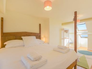 A bedroom with a wooden four-poster bed with white linens and towels a nightstand with a lamp and a small seating area near two skylight windows at Ottoline Cottage in Embleton