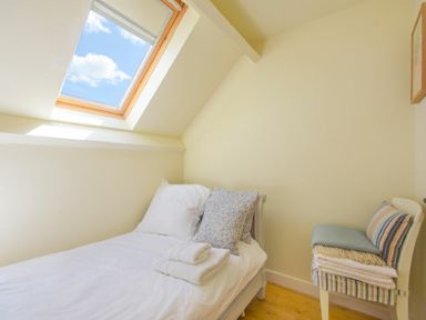 A small bedroom with a single bed next to a skylight window and a chair with folded linens at Ottoline Cottage Embleton