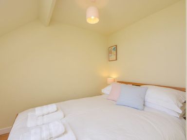 A bedroom with a bed with white linens and pillows a small lamp and a framed picture on the wall at Ottoline Cottage in Embleton