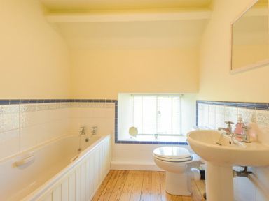 A bathroom with a bathtub toilet sink and a window with blinds at Ottoline Cottage in Embleton