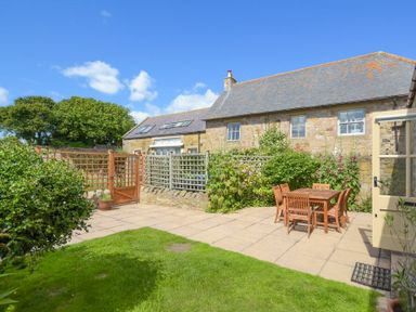 A stone house with a tiled roof and a patio with a wooden table and chairs in a garden at Ottoline Cottage in Embleton