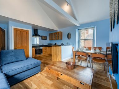 An open plan living room with a blue sofa wooden dining table and chairs and a kitchen with wooden cabinets at Pilots Rest in Alnmouth