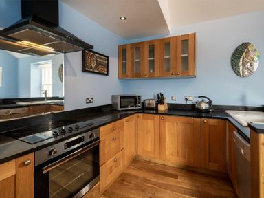 A kitchen with wooden cabinets a black countertop an oven a microwave a kettle and a toaster at Pilots Rest in Alnmouth