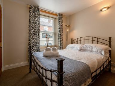 A bedroom with a double bed a window with patterned curtains and a floor lamp at Pilots Rest in Alnmouth