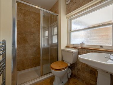 A bathroom with a shower, toilet with wooden seat, pedestal sink, and frosted window at Pilots Rest in Alnmouth