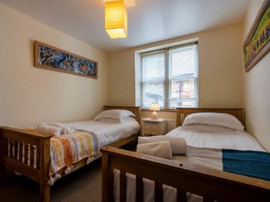 A bedroom with two single wooden beds a nightstand with lamp and artworks on walls at Pilots Rest in Alnmouth