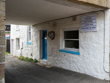 A covered passageway with a blue door and window with blue trim at Pilots Rest in Alnmouth
