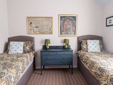 A bedroom with two single beds a blue dresser with two green lamps and framed artwork on the wall at Salty Dog in Bamburgh