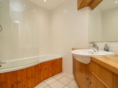 A bathroom with a bathtub that has a wooden panel and a sink with a wooden cabinet at Salty Dog in Bamburgh