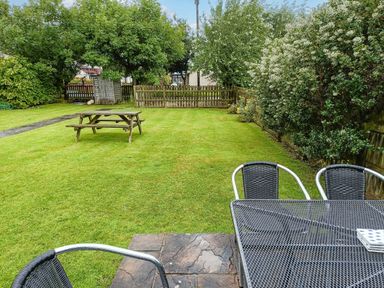 A backyard with a picnic table on grass and metal outdoor chairs around a table at Salty Dog in Bamburgh
