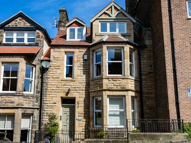 A stone house with bay windows and a green door between neighboring buildings at Upper Alnbank in Alnmouth