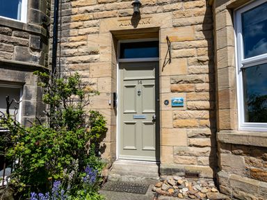 A front door with the number 14 on a stone building with plants and flowers at Upper Alnbank in Alnmouth