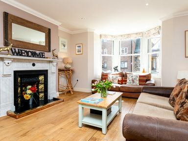 A living room with a fireplace coffee table with flowers two sofas and large windows at Upper Alnbank in Alnmouth
