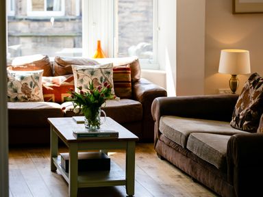 A living room with two sofas a wooden coffee table with flowers and books and a lamp on a side table at Upper Alnbank in Alnmouth