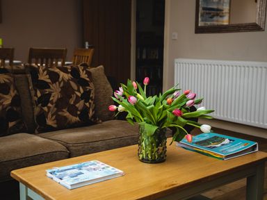A brown sofa with floral cushions and a wooden coffee table with a vase of tulips and books at Upper Alnbank in Alnmouth