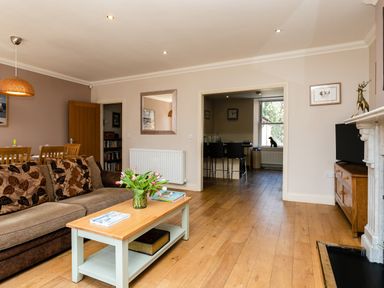A living room with a sofa coffee table flowers and dining table with chairs at Upper Alnbank in Alnmouth