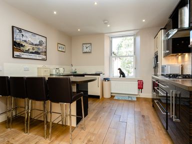 A kitchen with bar stools a window with a dog figurine and appliances at Upper Alnbank in Alnmouth