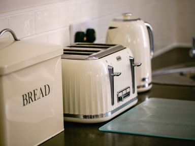 A kitchen counter with a bread box a four slot toaster a kettle and a glass cutting board at Upper Alnbank in Alnmouth
