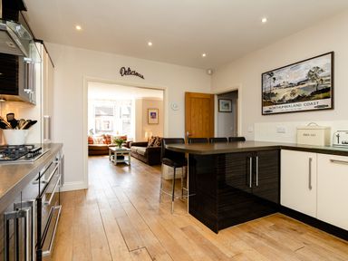A kitchen with an island and stools and a living room with sofas and a coffee table at Upper Alnbank in Alnmouth
