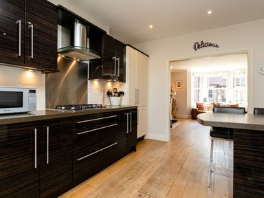 A kitchen with dark wood cabinets gas stove microwave and a breakfast bar with chairs at Upper Alnbank in Alnmouth