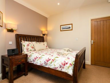 A bedroom with a wooden bed and floral bedding next to a wooden nightstand with a radio at Upper Alnbank in Alnmouth