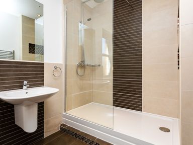 A bathroom with a wall-mounted sink and a walk-in shower with glass partition and tiled walls at Upper Alnbank in Alnmouth