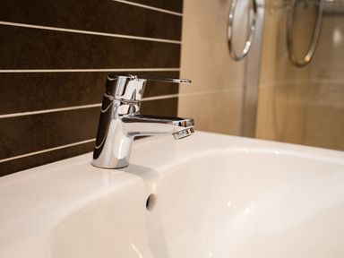 A bathroom sink with a chrome faucet and dark tiled wall at Upper Alnbank in Alnmouth