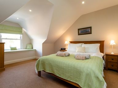 A bedroom with a bed covered with a green blanket and towels on top near a window with green checked cushions at Upper Alnbank in Alnmouth