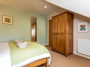 A bedroom with a wooden bed with towels on a green blanket and a wooden wardrobe with framed pictures on walls at Upper Alnbank in Alnmouth