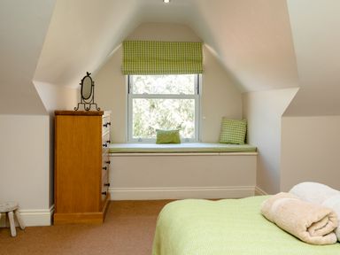 A bedroom with a wooden chest of drawers a cushioned window seat with green pillows and a bed with a folded blanket at Upper Alnbank in Alnmouth