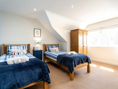 A bedroom with two single beds two rolled towels a blue bedside table a wooden wardrobe and a large window at Upper Alnbank in Alnmouth